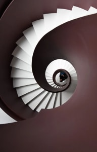 An upward view of a white spiral staircase with concrete steps and walls.