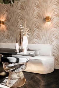 A modern living room featuring a fabric-covered sofa and metallic wire stool with a round table and sconce lighting.