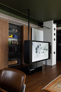 A modern living room featuring wooden walls and floor with a media console, a large screen displaying abstract art, and a lea