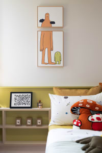 A modern bedroom featuring abstract art prints, plush pillows with mushroom designs, and a wooden shelf with decorative items