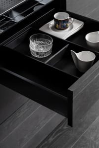 An open kitchen drawer showing black wooden compartments for dishes and cups.
