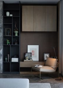 A modern living room featuring a black shelf with various decorative items, a beige armchair with a book, and a wooden cabine