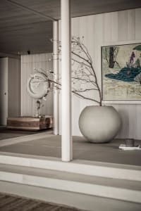 A minimalist interior design featuring a concrete vase with a bare branch and a framed painting hanging on the wall.
