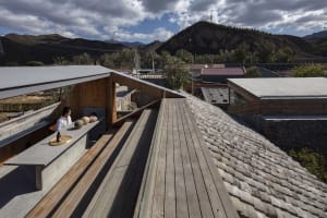 Modern building features a wooden roof with a skylight, set against a backdrop of mountains and cloudy sky.