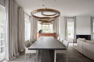 Modern dining room featuring natural wood dining table and chairs, with large windows, pendant lighting, and clean lines.