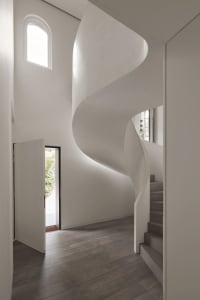 Modern interior design featuring a minimalist concrete staircase with natural light coming through an arched window.