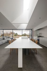Modern white concrete dining room with large windows and natural light.