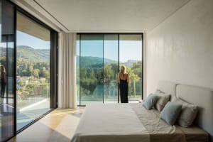 A modern bedroom with large glass windows overlooking green hills.