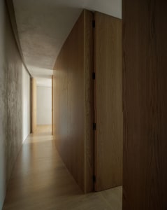 A minimalist hallway with curved wooden panels, natural light, and smooth walls.