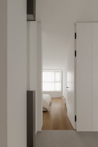 A minimalist bedroom with wood flooring and a bed.
