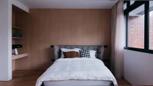 A minimalist bedroom featuring a bed with wooden headboard and white bedding, surrounded by wooden panels.