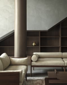 A modern living room with a textured wooden column, upholstered fabric seating, and dark wood shelves against a textured wall
