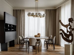 A modern dining room featuring a round wooden table and marble chairs, adorned with a decorative chandelier and abstract scul