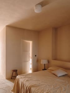 A minimalist bedroom with beige plaster walls and a simple bed setup.