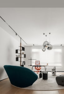 A minimalist home office featuring a sleek, metallic desk and orange chair, surrounded by contemporary decor and a large wind