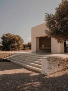 A modern architectural space with a concrete exterior, featuring a central open area surrounded by a stone wall and steps lea
