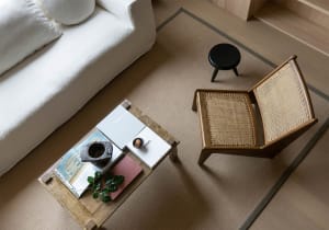 A living room with white sofa, woven armchair, coffee table, and black stool on a beige rug.