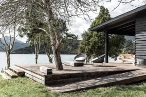 Modern minimalist patio with wooden deck, white cushions, and natural surroundings.
