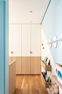 A modern children's room featuring white and light wood laminate cabinets, blue accents, and floating shelves.