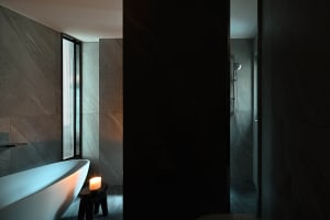 A modern bathroom with minimalist design, featuring a freestanding bathtub and a shower area with concrete tiles and a window