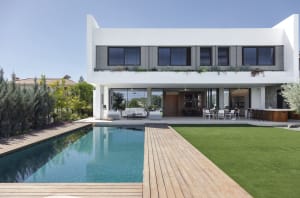 A modern residential house with a pool, wooden deck, and a green lawn.