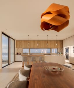 Modern residential kitchen with wooden cabinets and an open layout, featuring a large island with a waterfall countertop and 