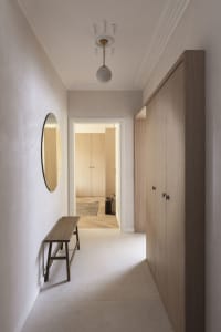 A minimalist corridor with wooden walls and floors, featuring a round mirror, a wooden bench, and a ceiling light fixture.