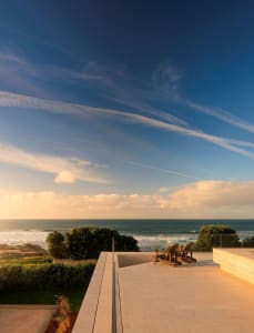 A minimalist luxury vacation resort features a stone terrace overlooking the ocean.