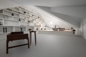 A minimalist living space with white walls, shelves, and furniture in white and dark wood.