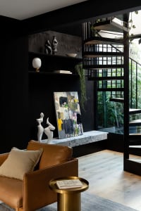 Modern industrial living room featuring a brown leather couch, wooden flooring, and a marble shelf with sculptures and art.