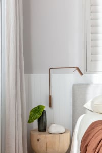 Modern bedroom featuring a wooden stool, a copper pendant lamp, and cotton linens.