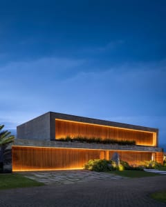 A modern minimalist house with concrete facade at night, illuminated by warm indoor lighting.