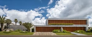 A modern, two-story concrete house with a green roof and landscaping.