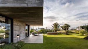 Modern house with concrete and glass exterior, featuring a garden view.