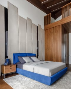 A modern bedroom featuring a blue velvet bed and wooden acoustic panels.