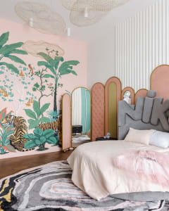 A modern bedroom featuring a tropical wall mural with palm trees and a tiger. The room has a grey upholstered bed with a pink