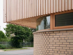 Modern architectural detail featuring a wooden exterior with curved windows and a wooden canopy.
