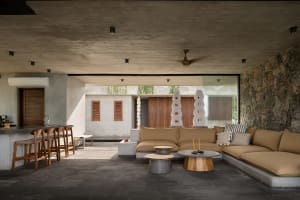 A modern living room with concrete walls and floor, featuring a large sectional sofa and minimalistic decor.