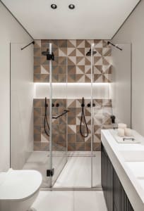 Modern bathroom with geometric patterned ceramic tiles on the wall, glass shower enclosure, and minimalist design elements.