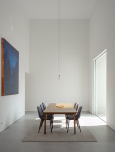 Modern minimalist dining room with a wooden table and chairs, featuring a large abstract painting and natural light streaming