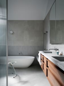 Modern minimalist bathroom featuring a grey concrete floor, grey tile walls, and a white bathtub.