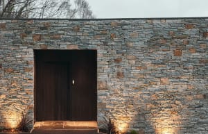 Modern entrance to a building with a stone exterior wall and a wooden door.