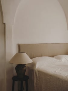 A minimalist bedroom featuring a bed with beige linen bedding and a ceramic lamp on a small side table.