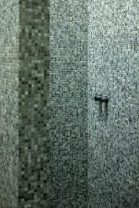Shower encased in green mosaic tiles with modern fixtures