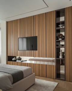 A minimalist bedroom with a brown paneled wall, a white bed with a gray blanket, and a floor-to-ceiling shelf with decorative