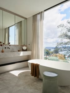 Modern minimalist bathroom featuring a marble bathtub and sink, with a large window showcasing an ocean view.