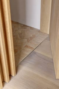A wooden floor meets ceramic tiles in a transitional corner, showcasing a seamless blend of natural and modern materials.