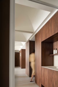 A minimalist corridor with wooden walls and a white ceiling. A person is seen entering a doorway in the background.