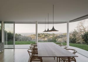 A minimalist outdoor dining area featuring a wooden table and chairs, with a view of the countryside.