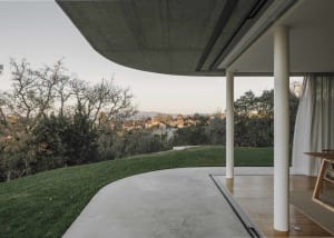 A modern residential outdoor area featuring a concrete patio, wooden deck, and greenery.